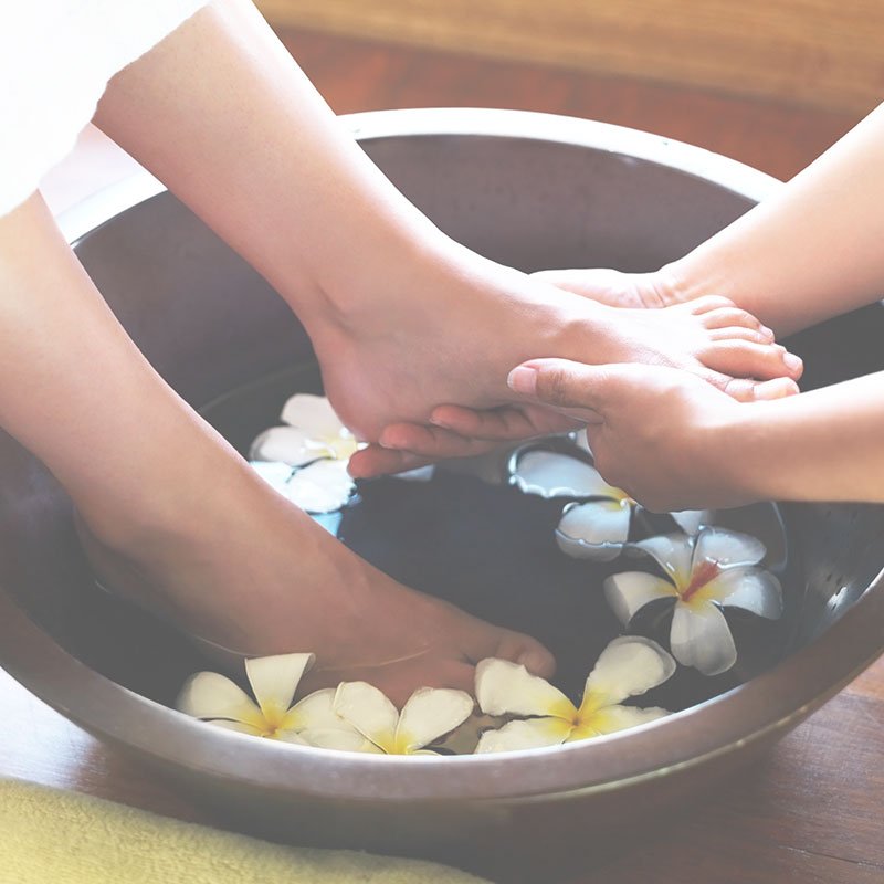 A woman receiving a pedicure from a beauty therapist, with her feet in a basin.